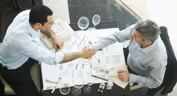 Two businessmen shake hands over a table. To lift potential growth, Italy needs to improve its business climate. (photo: Bob Burkany Cultura/Newscom)